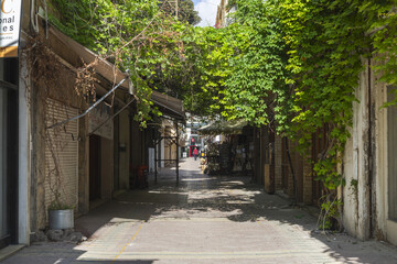 Lefkosia, Cyprus - 25 June 2025: View of a shadowed alleyway, where vibrant green vines cascade over aged brick buildings, creating a tunnel of light and shadow.