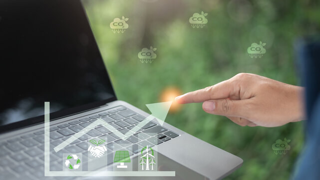 Close-up of a hand pointing at a laptop keyboard with a rising green graph, CO2 reduction icons, and clean energy symbols, representing sustainable growth and an eco-friendly technology strategy.