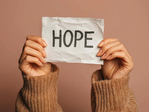 Uplift of 'Hope': A tender pair of hands delicately present a crumpled piece of paper, upon which the powerful word "HOPE" is inscribed, against a serene background. Evoking feelings of optimism.