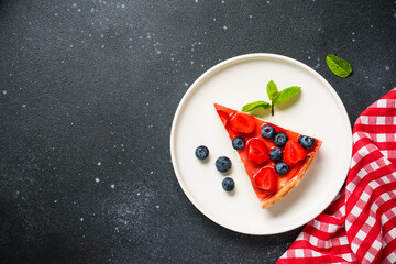Tart with strawberry and blueberry under jelly. Top view on black background with space for text.