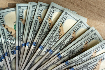 Fan of one hundred US dollar bills spread out on wooden surface in natural light. Concept of...