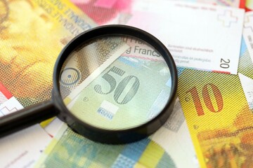 Swiss franc banknotes and magnifying glass. The current francs money bills with loupe lies on table