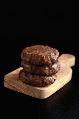 A perfectly cooked stack of three juicy burger patties rests on a rustic wooden cutting board...
