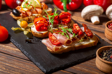 The photo features a black slate serving board with three pieces of toasted bread, each topped with different ingredients. The first piece is topped with smoked salmon, a lemon slice, a black olive