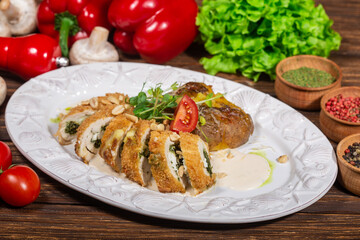. The plate contains sliced, breaded chicken rolls stuffed with spinach and cheese, garnished with microgreens, a tomato slice, and sprinkled with peanuts.