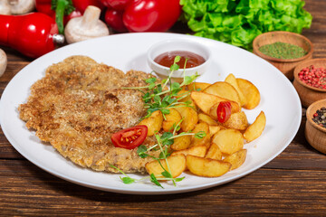 The photo shows a plate of food served on a wooden table. The dish includes a breaded cutlet,...