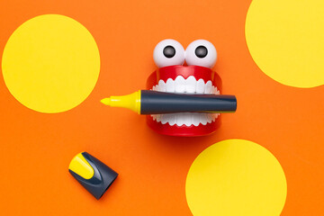 Playful Red Chattering Teeth and Yellow Marker on Bright Orange Background