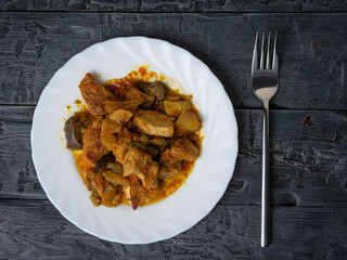 Rustic Meal Featuring Roasted Vegetables and Meat on White Plate with Fork on Wooden Table