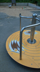 Modern playground with yellow slide and black tunnel tube structure in urban park. Sunny day, city skyscrapers in background. Children's outdoor play area