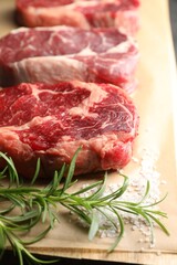 Pieces of raw beef meat, rosemary and salt on table, closeup