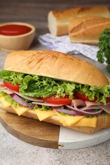 Tasty baguette sandwich with ham, cheese and vegetables on grey textured table, closeup