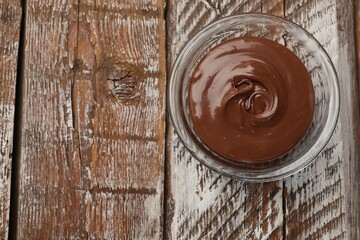 Tasty chocolate butter in glass bowl on color wooden table, top view. Space for text