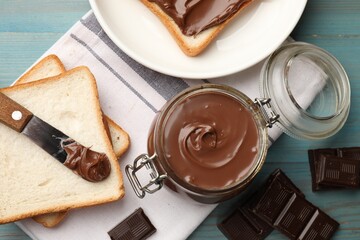 Tasty chocolate butter in jar, pieces, knife and bread on light blue wooden table, flat lay