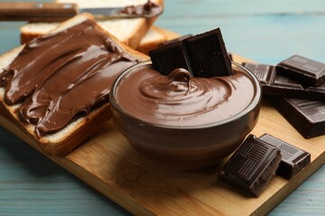 Tasty chocolate butter in bowl, pieces and bread on light blue wooden table, closeup
