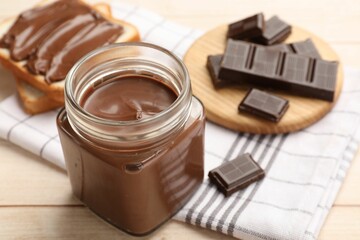 Tasty chocolate butter in glass jar, pieces and sandwiches on wooden table, closeup