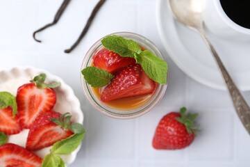 Tasty panna cotta with caramel, strawberries, mint, vanilla pods and coffee on white tiled table, flat lay