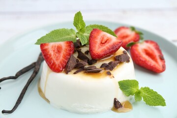 Tasty panna cotta with chocolate, strawberries, mint, caramel and vanilla pods on table, closeup
