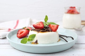 Tasty panna cotta with chocolate, strawberries, mint, caramel and vanilla pods on white wooden table, closeup