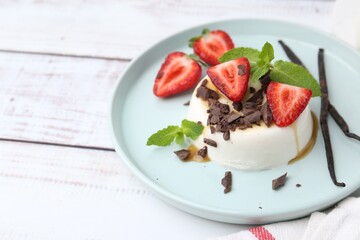 Tasty panna cotta with chocolate, strawberries, mint, caramel and vanilla on white wooden table, closeup. Space for text