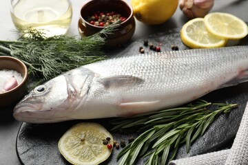 Fresh raw seabass with spices on grey table, closeup. Fish and seafood delicacies
