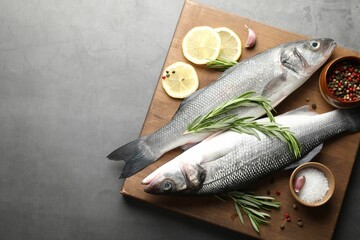 Fresh raw seabass fish with spices on grey table, top view and space for text. Seafood delicacies