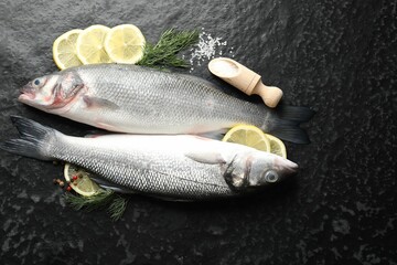 Fresh raw seabass with spices on black table, flat lay. Fish and seafood delicacies