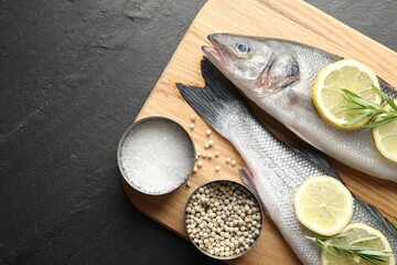 Fresh raw seabass fish with spices on black table, top view and space for text. Seafood delicacies