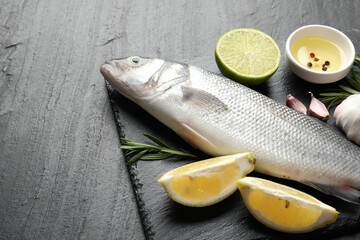Fresh raw seabass with spices on black table, closeup. Fish and seafood delicacies