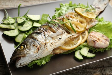 Tasty roasted seabass fish served with vegetables and lemon on wooden table, closeup. Homemade...