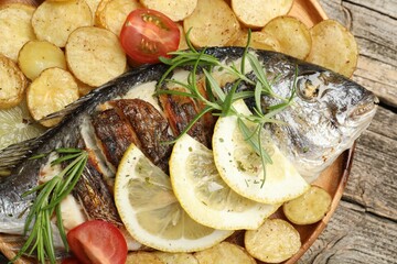 Tasty roasted dorado fish served with potatoes, tomatoes and lemon on wooden table, top view. Homemade seafood dish