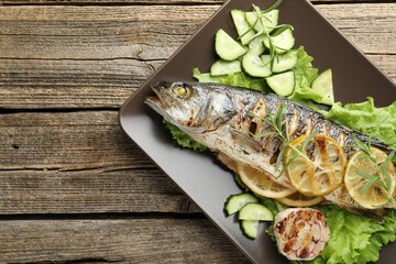 Tasty roasted seabass fish served with vegetables and lemon on wooden table, top view and space for...