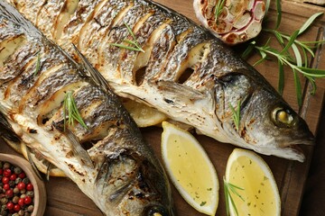 Tasty roasted seabass fish served with rosemary and lemon on wooden table, flat lay. Homemade seafood dish