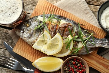 Tasty roasted dorado fish served with rosemary and lemon on wooden table, flat lay. Homemade seafood dish