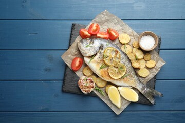 Homemade seafood dish. Tasty roasted dorado fish with vegetables and spices on blue wooden table, flat lay. Space for text