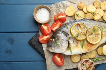 Homemade seafood dish. Tasty roasted dorado fish with vegetables and spices on blue wooden table,...