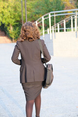 Executive woman in black suit walking away from office building
