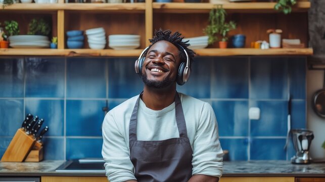 Happy man wearing wireless headphones and listening to music in kitchen - Powered by Adobe