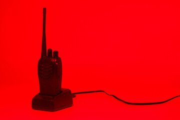 Unique black walkie talkie on a red background with a power cord visible in a minimalist setup for...