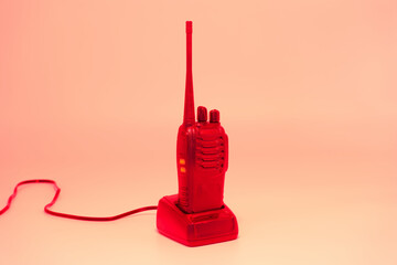 Bright red walkie talkie resting on its charger against a plain backdrop, showcasing a vintage...