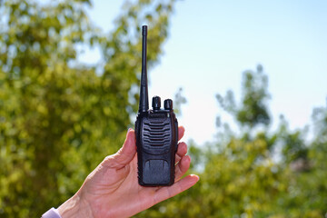 Handheld walkie talkie being held against a sunny outdoor background with greenery