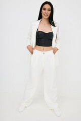 smiling woman wearing white wide pants and blazer with black crop top stands confidently with hands...