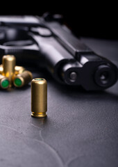 Close-up of a handgun and several bullets on a dark surface. The focus is on a single brass...
