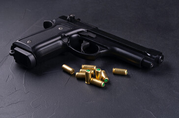 Black semi-automatic pistol with a textured grip lies on a dark surface next to several...