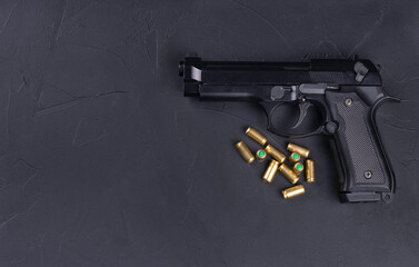 Close-up image of a black semi-automatic handgun and several brass bullets arranged on a dark...