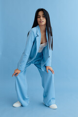 Young woman wearing a light blue suit poses confidently against a matching blue background,...