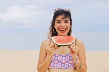 Asian woman having fun on a tropical beach and holding watermelon slices on their heads.
