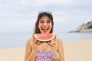 Asian woman having fun on a tropical beach and holding watermelon slices on their heads.
