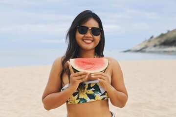 Asian woman having fun on a tropical beach and holding watermelon slices on their heads.