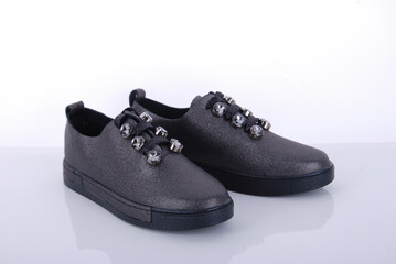 Stylish black sneakers with decorative elements displayed on a white surface for a modern footwear showcase