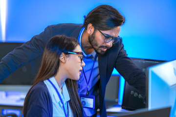 Asian female AI programmer and Indian male data analyst reviewing code on a monitor. Diverse tech...